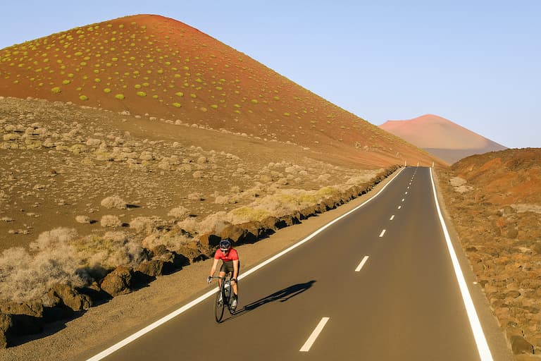 Radfahrer auf einer Küstenstraße in Lanzarote mit Vulkanlandschaft im Hintergrund